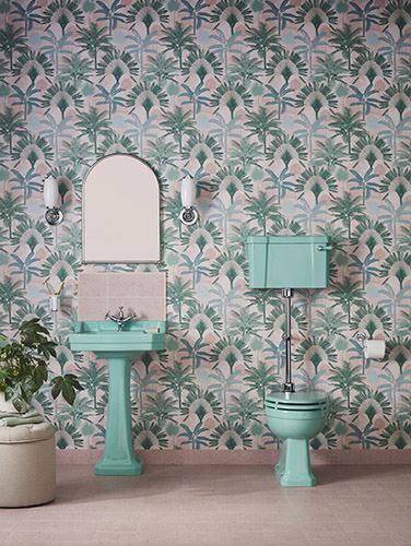 A striking pink, green and blue wallpaper featuring various trees add a bold backdrop to the powerful colours of the ceramic basin and toilet in this colourful bathroom. Bespoke by Burlington Cosmic Green bathroom ceramics